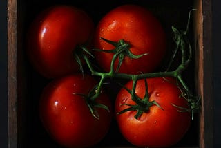 4 deep red tomatoes on the vine in a thin wooden box