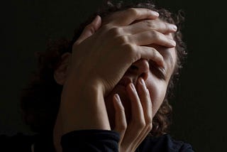 woman’s face mostly covered by her hands, looking stressed