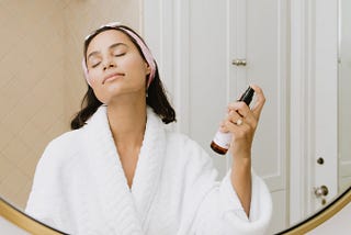 A woman in a bathrobe using a natural skincare product.