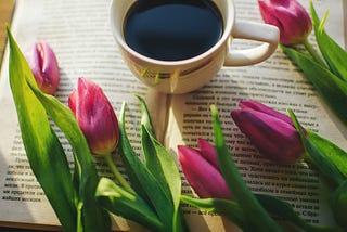 a white cup of black coffee surrounded by beautiful lillat flowers on an open book