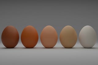Five eggs sit upright against a grey background, their colours ranging from dark tan on the left to stark white on the right.