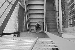 Person sitting in the middle of many sets of stairs