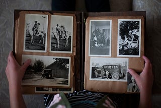 An old photo album opened on black and white pictures. On the right page, two vertical pictures of people on horses and a horizontal picture of a cabin. On the left page, two vertical pictures of people and a horizontal picture of two kids in front of an old car.