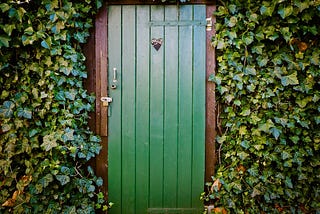 An image of a green door, surrounded in foilage