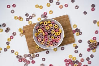 Bowl of Fruit Loops on wood board with Fruit Loops scattered around bowl