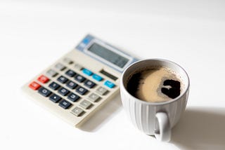 A calculator and a cup of coffee sit side-by-side.