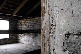 A glimpse inside a concentration camp prisoner barracks. You can see the flat wooden surface they were expected to sleep on, and a Star of David is drawn beside the doorframe in chalk.