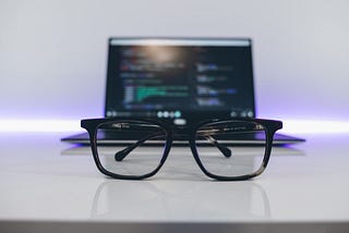 A pair of glasses in front of an open laptop