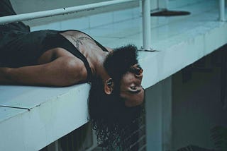 A bearded man lying on a ledge with a distant expression, symbolizing disconnection and emotional fatigue