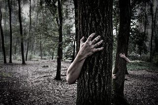 Black and white image of a tree with a hand and arm coming around it