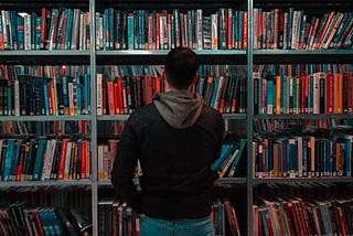 man standing in front of a filled book shelf