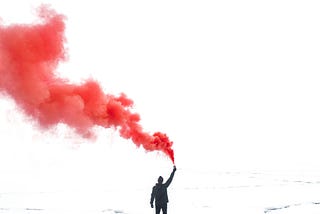 Man standing on some island with a red smoke emission in his hand