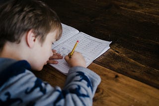 A young child sits hunched over while filling out a school workbook.