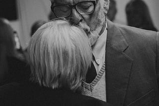 elderly man kissing a woman’s forehead while dancing