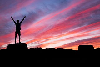 A driven person standing on top of the hill with arms up