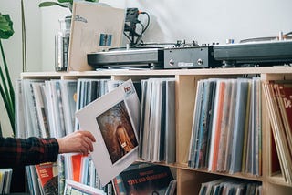 Uma pessoa retirando um disco de vinil de uma prateleira com vários outros discos