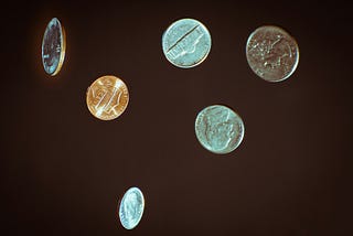 Several coins, including two nickels, a dime, a penny, and two quarters, fall from the sky.