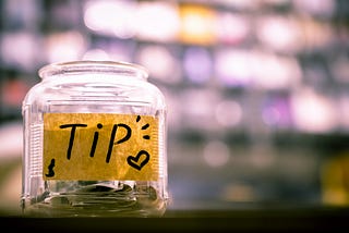 Glass jar with tip sign sits on a table.