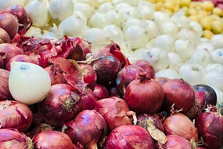 looking close-up at a grocery store shelf of red, white and yellow onions