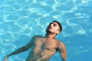 sexy man floating in a swimming pool, eyes closed