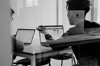 Black & white photo of 2 people meeting at their laptops.