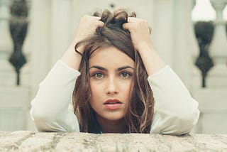 A woman bunching up her hair on her head with her hands as she looks nervously into the camera.