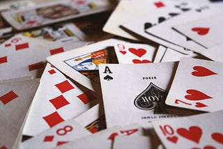 A deck of cards is spread across a table. On top, an ace of spades is visible.