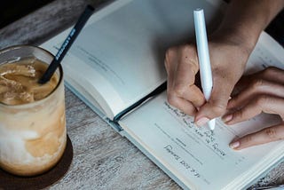 Photo of woman writing in a journal with ice coffee