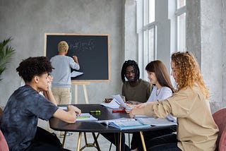 Anonymous man writing on chalkboard near group of diverse students at table