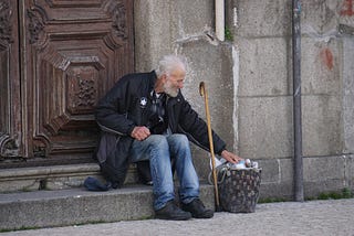 Old man resting on the steps of a church with his cane and bag of belongings