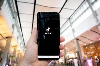 A person’s hand holding a smartphone showing the TikTok app opening screen.