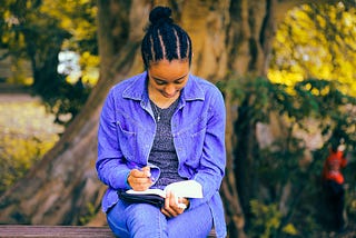 A woman sits on a bench writing in her book or journal