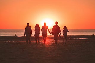 a group of people walk towards a sunset on a beach