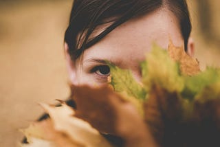 A little girl’s face half hiding behind leaves. She looks angry or suspicious