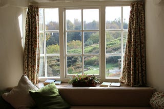 a large window with a desk in front of it. lots of trees and grass and sunshine