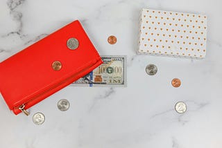 An image of a purse with a few scattered coins and a hundred-dollar bill nearby.