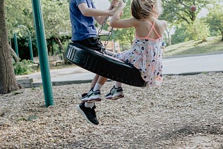 Two children sit on a tire swing.