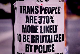 sticker on a pole beneath a smaller one that reads: jesus loves you reads in bold black letters against white: trans people are 370% more likely to be brutalized by police than cis people.