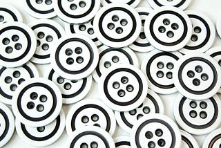 A set of black-and-white coat buttons scattered on a white surface