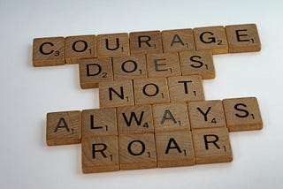 scrabble tiles spelling out the phrase ‘courage does not always roar’