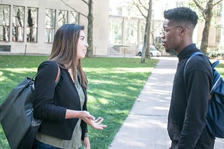 A young man and a young woman speaking to each other.