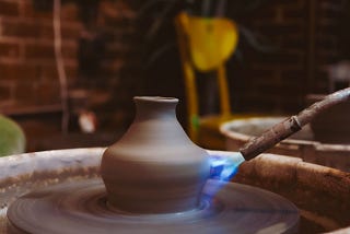 gas torch firing an unfinished vase-shaped pottery piece. the blurry vase and wheel it stands on shows that it is spinning.