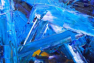 A close up of paint on a canvas with shades of primarily blue, but also white, yellow, and purple. The paint is applied in wide frenzied strokes. The texture of the paint on the canvas is very prominent.