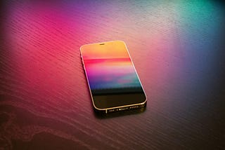 This is a photo of an iphone with a colorful screen, sitting on a background that is alsio colorful, mostly reds and pink.