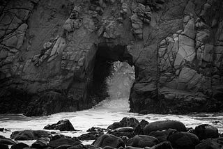 A beachside outcarving of rock with water splashing through it.
