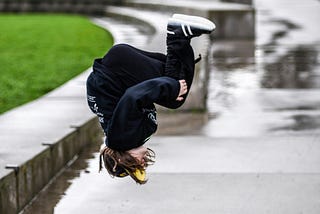 Young person somersaulting on a wet sidewalk