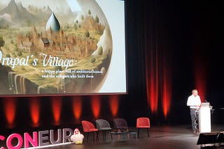 Dries presenting his Driesnote (keynote) — Slide is of a stylized Drupal Village.