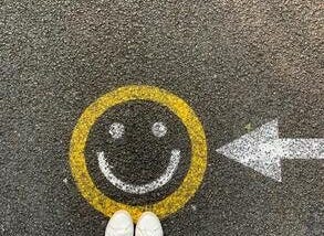 Yellow circle drawn with chalk on black asphalt, with white eyes and smile inside the yellow circle.