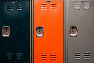 Three school lockers. One black, one orange, and one gray.