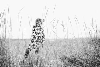 a grayscale photo of a woman looking out over a field